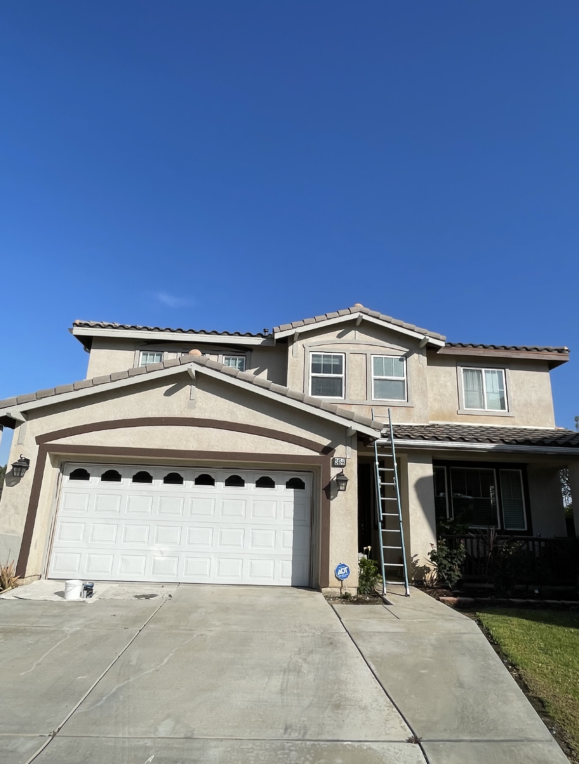 Two-story stucco home prepped for repaint with ladder at the entry
